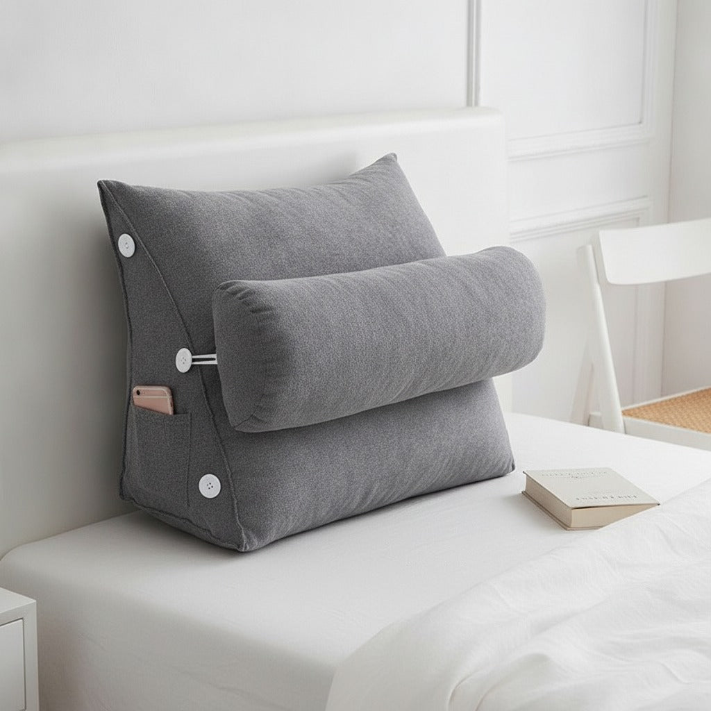 Coussin dossier triangulaire gris posé contre une tête de lit, livre à côté (mise en situation illustrative)