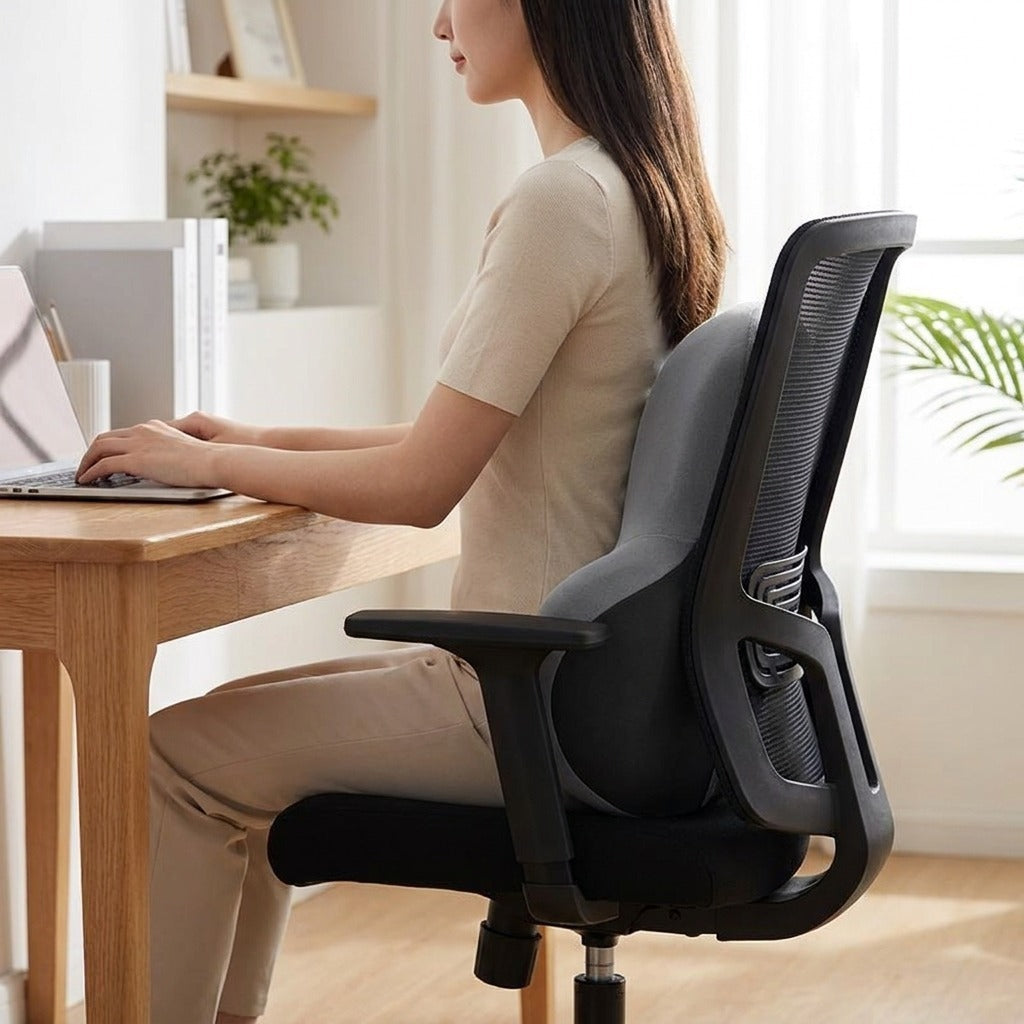 Femme assise au bureau, le coussin lombaire gris calé contre le dossier de sa chaise