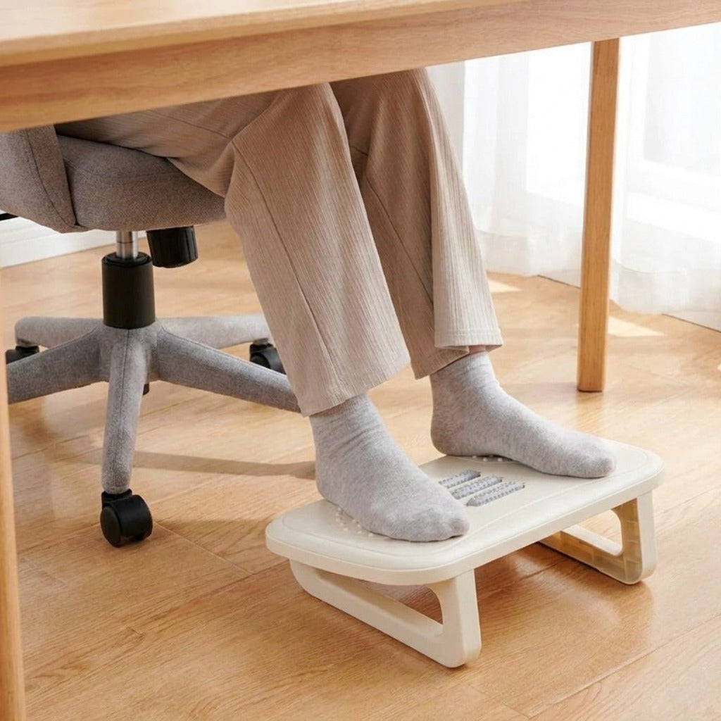 Pieds en chaussettes posés sur le repose-pieds incliné, sous un bureau en bois