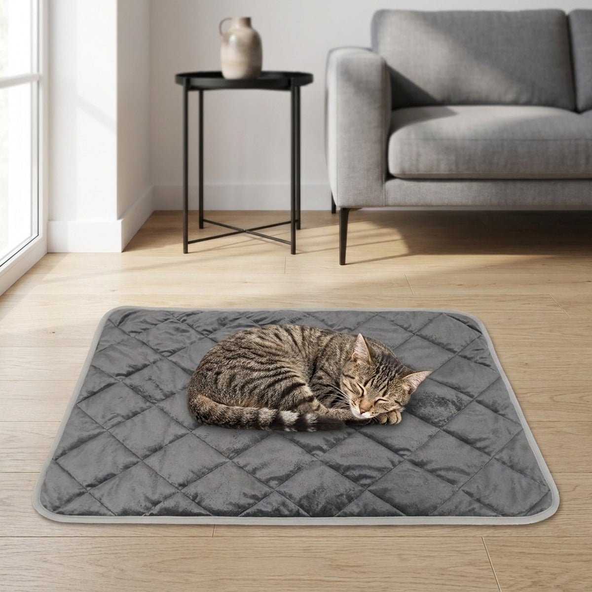 Un chat endormi sur le tapis auto-chauffant gris, posé sur un parquet clair