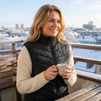 Mise en situation : femme buvant un café sur un balcon en hiver, gilet chauffant noir sur un pull crème