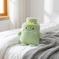 Bouillotte peluche dinosaure vert posée sur un lit blanc et un plaid gris