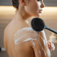 Femme utilisant la brosse pour le dos en silicone DermaScrub™, créant une mousse riche pour un nettoyage en douceur de l'épaule.