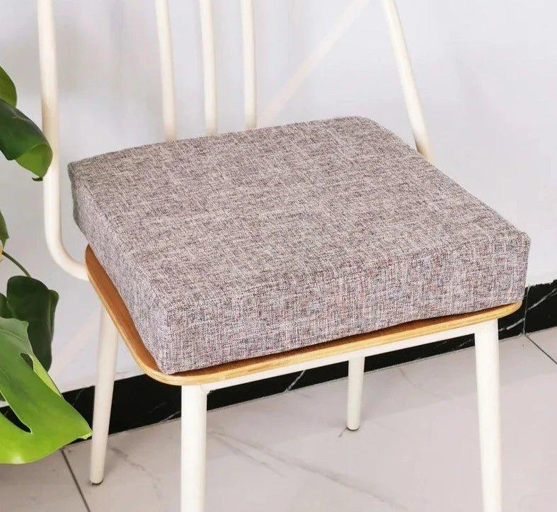Coussin carré épais gris clair posé sur une chaise à structure blanche