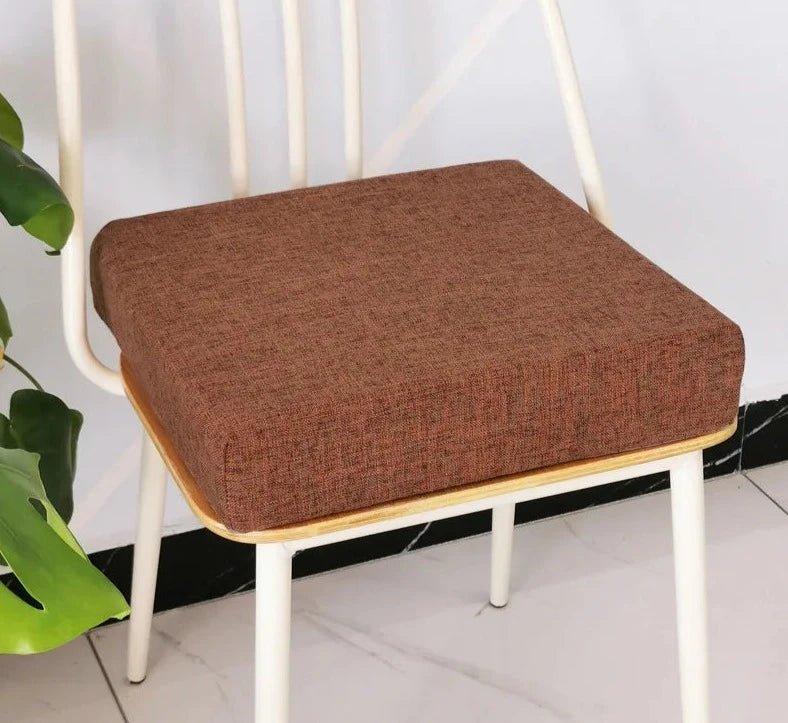 Coussin carré épais café posé sur une chaise à structure blanche