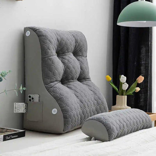 Dossier incliné matelassé gris avec poche latérale et coussin cylindrique posé sur un lit