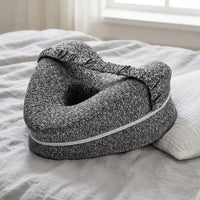 Coussin entre-genoux gris posé sur un lit à côté d’un oreiller — mise en situation illustrative