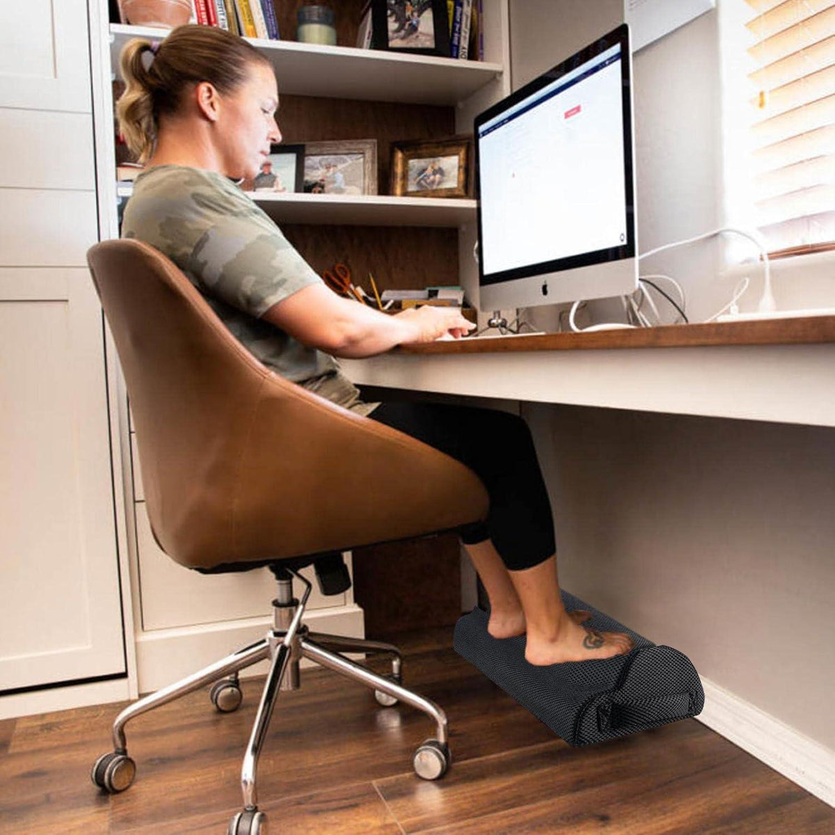 Personne assise à un bureau avec les pieds posés sur un coussin noir