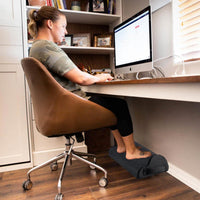 Personne assise à un bureau avec les pieds posés sur un coussin noir