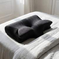 Oreiller DreamContour noir posé sur un lit au linge gris clair — mise en situation illustrative